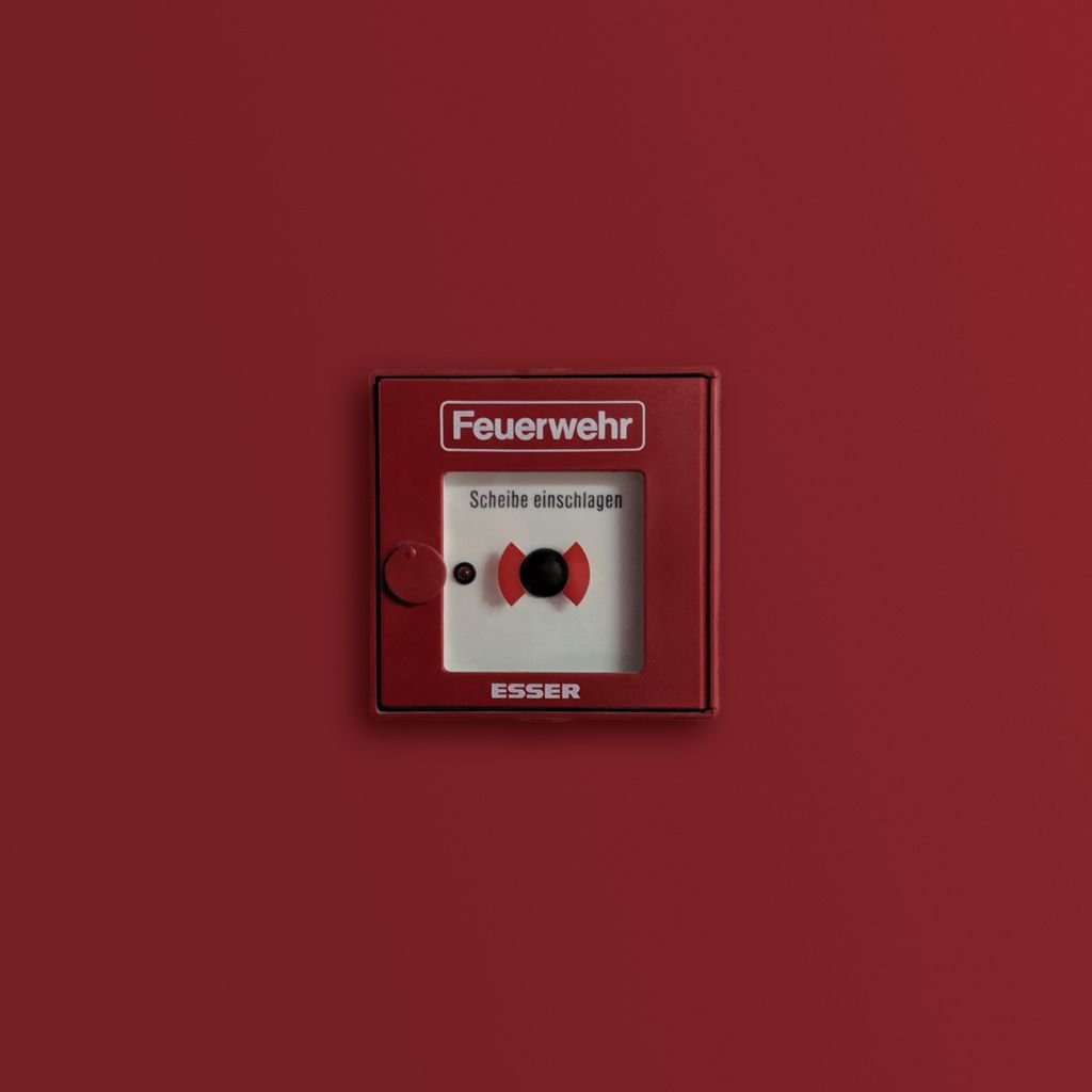 Red fire alarm panel indicating emergency system on solid background.